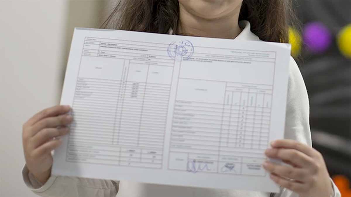 Kısa Karne Tebrik MesajlarıElinde karne tutan bir çocuk, karneyi kameraya gösteriyor.